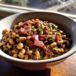 A bowl of black eyed peas recipe crock pot, topped with crispy bacon and fresh herbs.