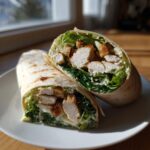 A chicken ceasar wrap cut in half, showing the chicken, lettuce, croutons, and dressing filling.