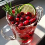 Close-up of a Christmas mocktail non alcoholic with cranberries, lime, and rosemary in a glass mug.