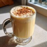 A glass mug filled with creamy eggnog recipe, topped with foam and a sprinkle of cinnamon.
