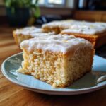 A slice of iced lemon dessert cake on a blue plate, showcasing its moist texture and lemon zest garnish. A perfect lemon desserts treat.