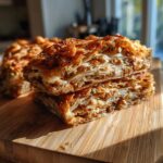 Two slices of a layered phyllo dough recipes dessert stacked on a wooden board, showcasing flaky layers and filling.