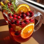 A pitcher of winter mocktails non alcoholic with cranberries, orange slices, lime, and rosemary garnish.