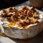 Close-up of baked brie cheese topped with nuts and honey, dripping down the sides.