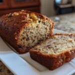 A loaf of banana bread with a slice cut, showcasing the moist texture and ingredients.