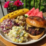 A delicious plate of food featuring a burger, corn on the cob, potato salad, coleslaw, and watermelon, perfect for BBQ baby shower ideas.