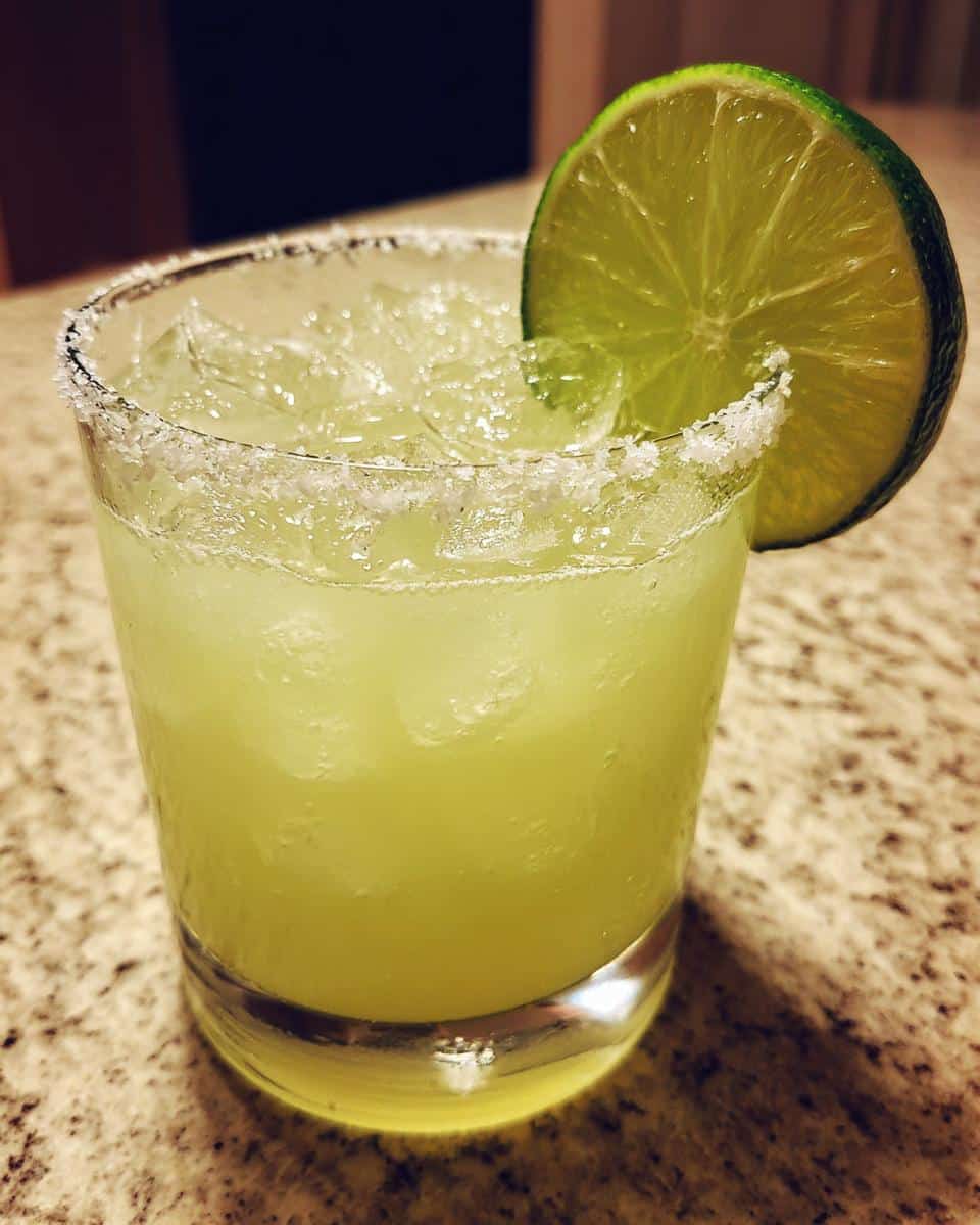 A glass of best margarita recipe with ice, salted rim, and lime wedge garnish.