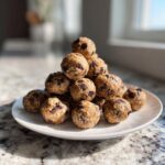 A stack of homemade protein balls with chocolate chips on a white plate, ready to eat.