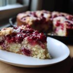 A slice of Crock Pot Dump Cake on a white plate, topped with cherries. The rest of the cake is visible in the background.