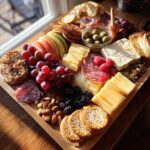 A beautifully arranged charcuterie board featuring a variety of cheeses, meats, fruits, crackers, and nuts.