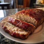 A freshly baked meatloaf with a glazed top, sliced and served on a plate. Delicious meatloaf recipe.