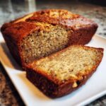 A sliced loaf of Gluten Free Banana Bread on a white plate, showcasing its moist texture and golden crust.