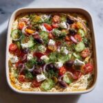 Overhead shot of a vibrant Greek Layer Dip with feta, tomatoes, cucumbers, olives, and red onion.