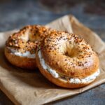 Two homemade Greek yogurt bagels filled with cream cheese, sitting on parchment paper.