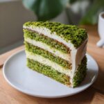 A slice of layered green cake, a delicious example of green foods for party, with white frosting on a white plate.
