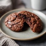 Two Healthy Chocolate Cookies on a plate, one broken in half to show the soft inside.