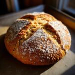 Close-up of a freshly baked loaf of Irish soda bread, dusted with flour, showing its golden-brown crust.