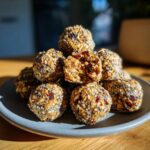 A stack of homemade oatmeal protein balls on a gray plate, showing oats, seeds, and dried fruit.