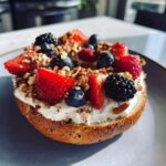 A protein bagel with greek yogurt, topped with fresh strawberries, blueberries, raspberries, and blackberries.