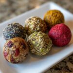 Assortment of colorful protein balls no bake on a white plate, showcasing different coatings and ingredients.