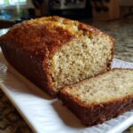 A loaf of sourdough discard banana bread with a slice cut, showcasing the moist texture.