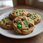 Four St Patrick’s Day cookies with green candies and chocolate chips on a white plate.
