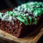 Close-up of a brownie slice, a festive St Patrick’s Day treat, with green frosting and chocolate drizzle.