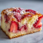 Close-up of a slice of Strawberry Dump Cake, topped with fresh strawberries and a dusting of powdered sugar.