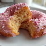 Two air fryer heart donuts, one broken in half, glazed with pink icing and sprinkles.