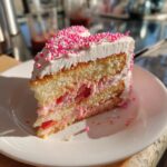 A slice of heart-shaped layer cake, a gluten-free Valentine dessert, with pink frosting and sprinkles.