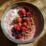 Overhead shot of a healthy pink smoothie bowl topped with fresh berries, coconut flakes, and granola.