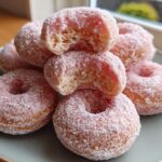 A stack of pink frosted mochi donut minis, one with a bite taken out, on a blue plate.