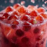 Close-up of a vibrant Strawberry boba drink with boba pearls, ice, and condensation on the glass.