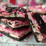 A stack of Valentine's Oreo bark pieces topped with an Oreo and festive sprinkles.